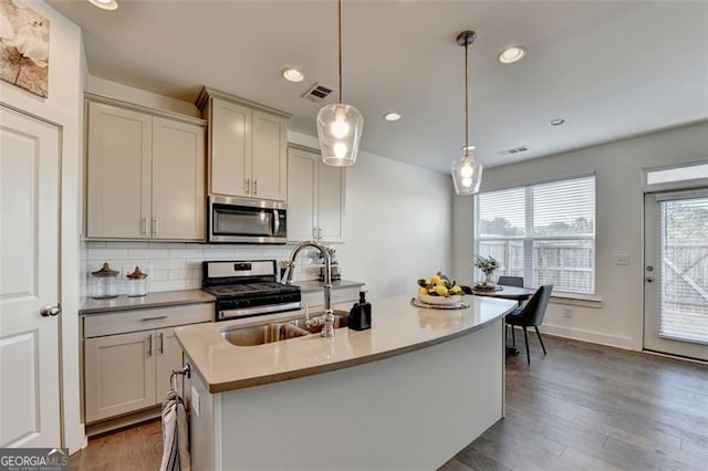 kitchen with sink, stainless steel appliances, backsplash, pendant lighting, and a center island with sink