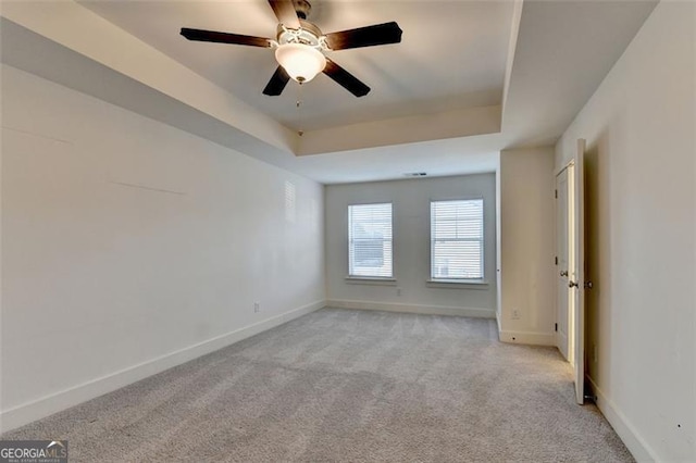 empty room with a tray ceiling, ceiling fan, and light colored carpet