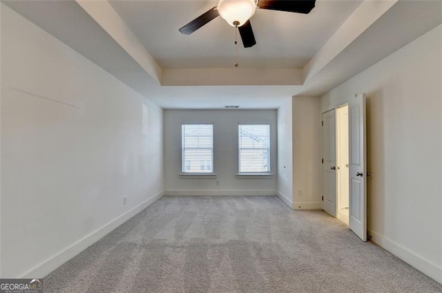 unfurnished room featuring a raised ceiling, ceiling fan, and light carpet