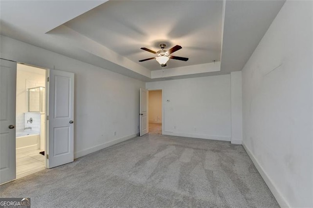 carpeted empty room with a raised ceiling and ceiling fan