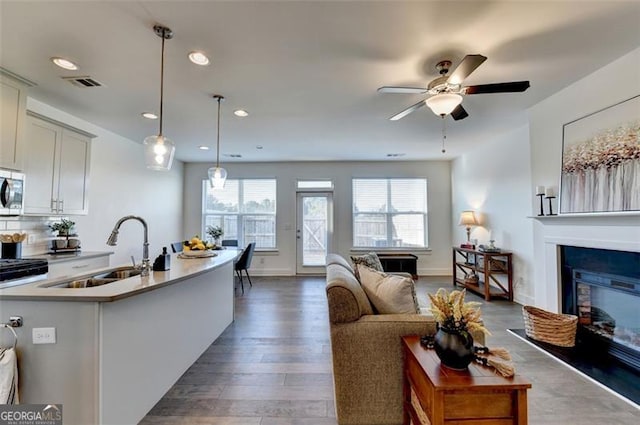 kitchen with a center island with sink, sink, ceiling fan, decorative light fixtures, and dark hardwood / wood-style flooring