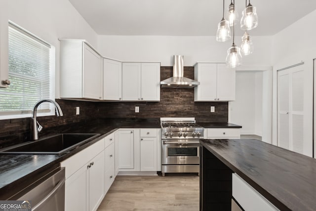 kitchen with wall chimney range hood, sink, hanging light fixtures, white cabinetry, and stainless steel appliances