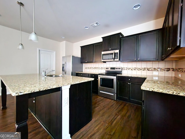 kitchen featuring tasteful backsplash, stainless steel appliances, a kitchen island with sink, decorative light fixtures, and dark hardwood / wood-style floors