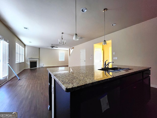 kitchen with sink, ceiling fan, an island with sink, decorative light fixtures, and light stone counters