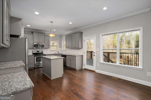 kitchen featuring crown molding, light stone countertops, appliances with stainless steel finishes, decorative light fixtures, and a kitchen island