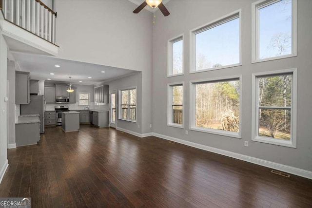 unfurnished living room featuring a towering ceiling, dark hardwood / wood-style floors, ceiling fan, and a healthy amount of sunlight