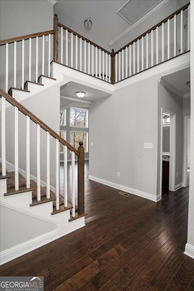 stairway with wood-type flooring, crown molding, and a high ceiling