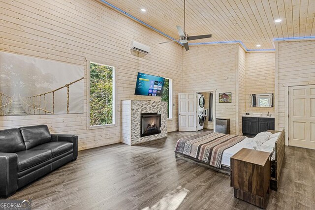 bedroom with ceiling fan, high vaulted ceiling, stacked washer / dryer, wood walls, and wood ceiling