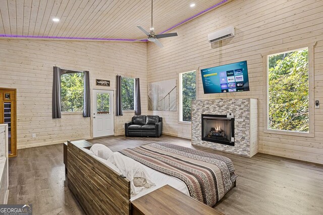 bedroom with ceiling fan, a stone fireplace, high vaulted ceiling, wood walls, and hardwood / wood-style floors