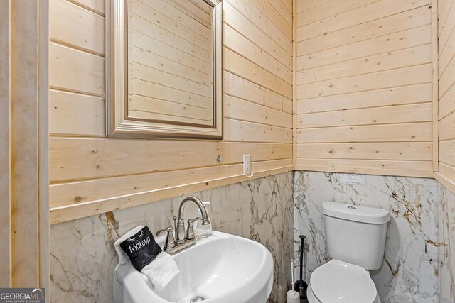 bathroom featuring toilet, sink, and wooden walls