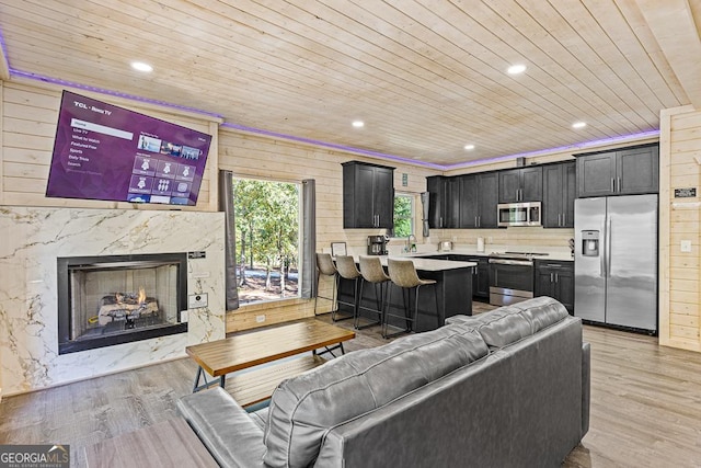 living room with sink, light hardwood / wood-style flooring, wooden ceiling, a fireplace, and wood walls