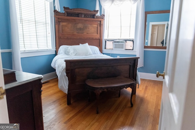 bedroom with cooling unit, light wood-type flooring, and multiple windows