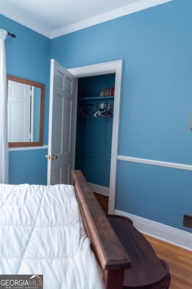 bedroom featuring hardwood / wood-style flooring, crown molding, and a closet