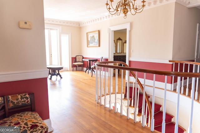 stairway with hardwood / wood-style flooring, crown molding, and a notable chandelier