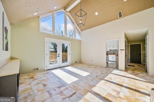 interior space with french doors, a healthy amount of sunlight, an inviting chandelier, and high vaulted ceiling