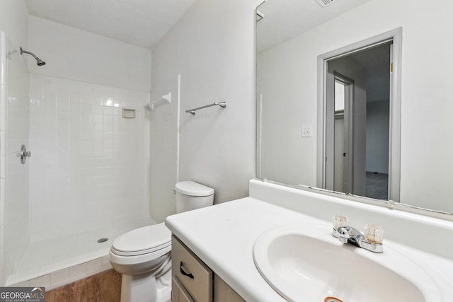 bathroom with toilet, vanity, wood-type flooring, and a tile shower