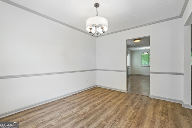 unfurnished room with an inviting chandelier, ornamental molding, and hardwood / wood-style flooring