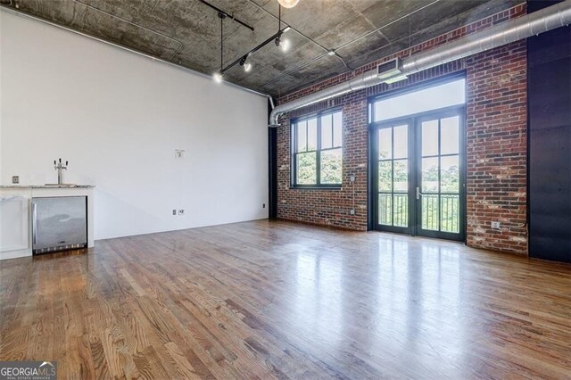 unfurnished living room featuring hardwood / wood-style floors, french doors, and brick wall