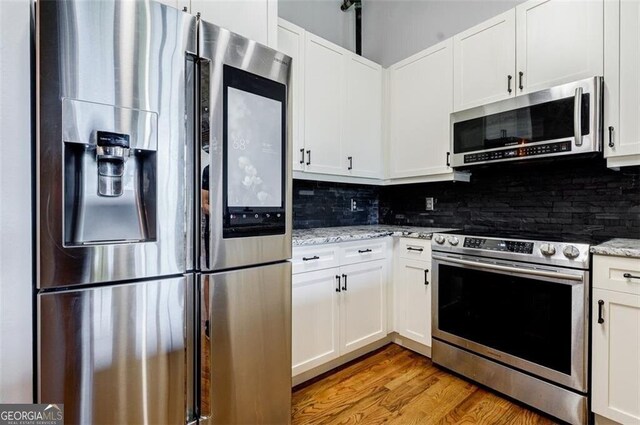 kitchen with stainless steel appliances, light stone counters, light hardwood / wood-style flooring, decorative backsplash, and white cabinets