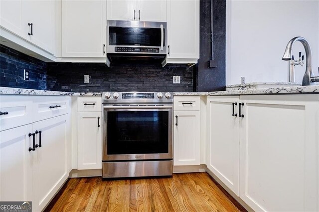 kitchen with white cabinets, backsplash, light stone counters, and stainless steel appliances