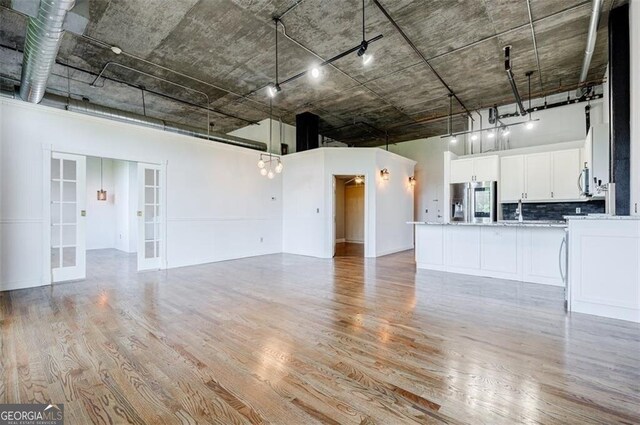 unfurnished living room with light hardwood / wood-style flooring, a towering ceiling, and french doors