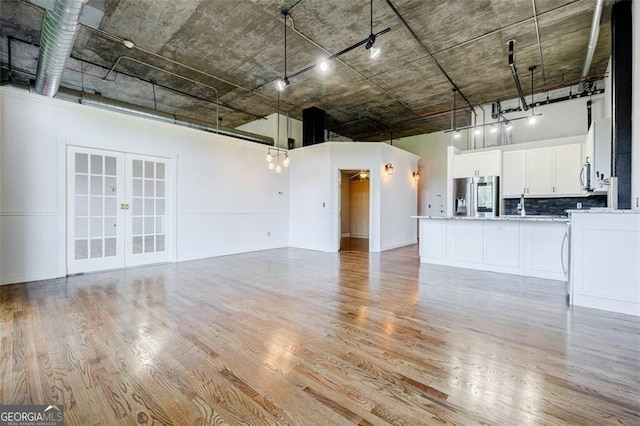 unfurnished living room featuring french doors, a high ceiling, and light wood-type flooring