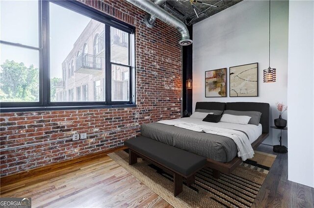 bedroom with hardwood / wood-style flooring, a high ceiling, and brick wall