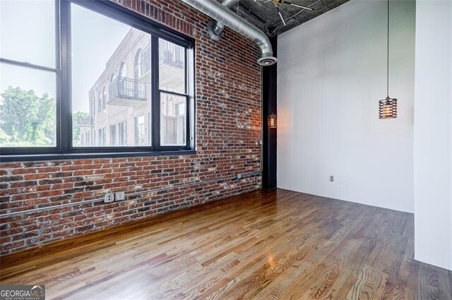 empty room with hardwood / wood-style flooring, plenty of natural light, and brick wall