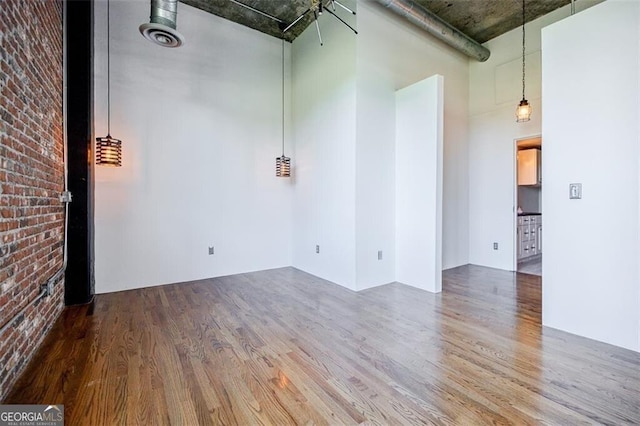 empty room featuring hardwood / wood-style floors, a towering ceiling, and brick wall