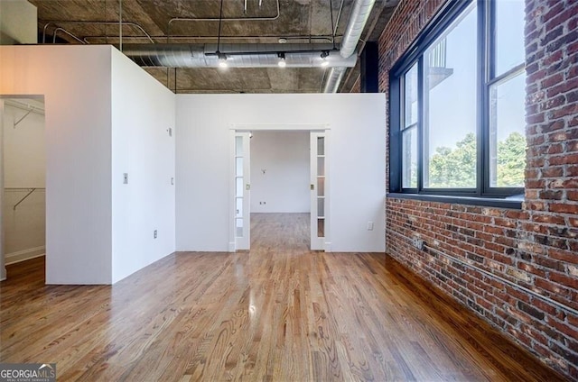 spare room with hardwood / wood-style floors, track lighting, and brick wall