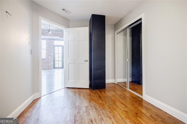 unfurnished bedroom featuring hardwood / wood-style flooring, a closet, and brick wall