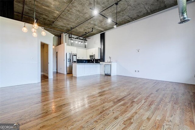 unfurnished living room featuring light wood-type flooring, sink, and a towering ceiling