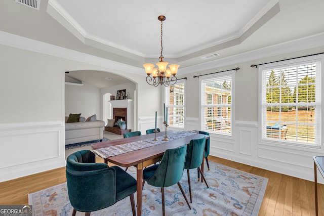 dining space with hardwood / wood-style floors, a raised ceiling, crown molding, and a notable chandelier