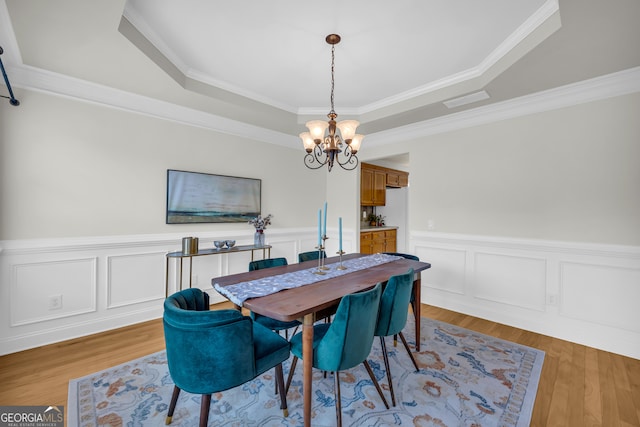 dining area with a tray ceiling, light hardwood / wood-style floors, a notable chandelier, and ornamental molding