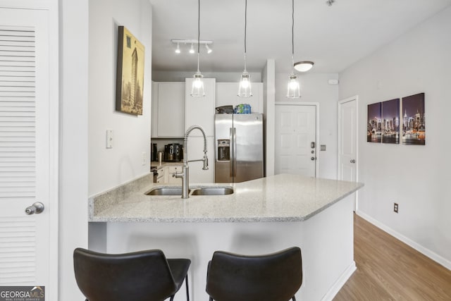 kitchen featuring sink, hanging light fixtures, stainless steel fridge, white cabinetry, and kitchen peninsula