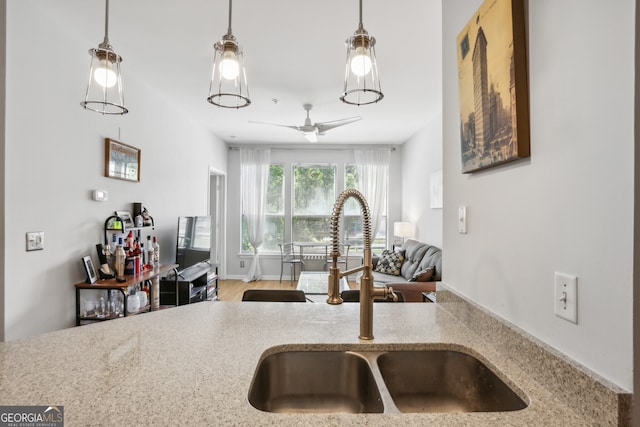 kitchen featuring ceiling fan, light stone counters, sink, and decorative light fixtures