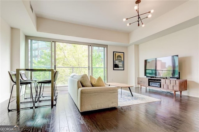 living room with a raised ceiling, dark hardwood / wood-style flooring, and an inviting chandelier