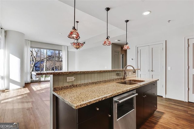 kitchen featuring dishwasher, sink, hanging light fixtures, wood-type flooring, and a center island with sink