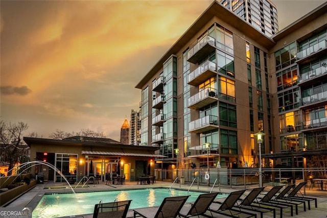 pool at dusk featuring a patio and pool water feature