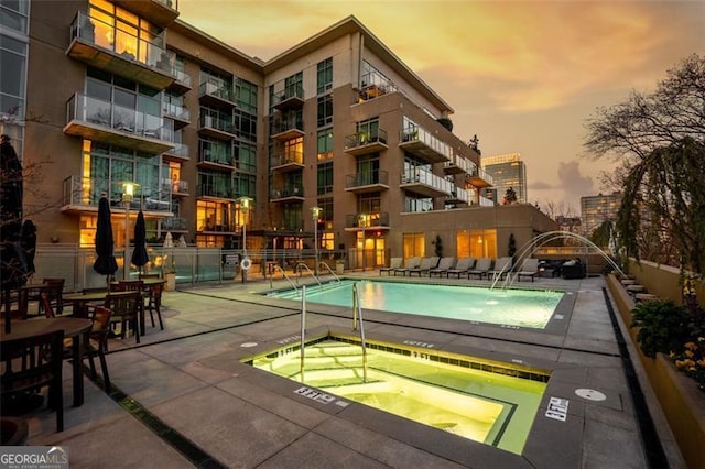 pool at dusk with a hot tub