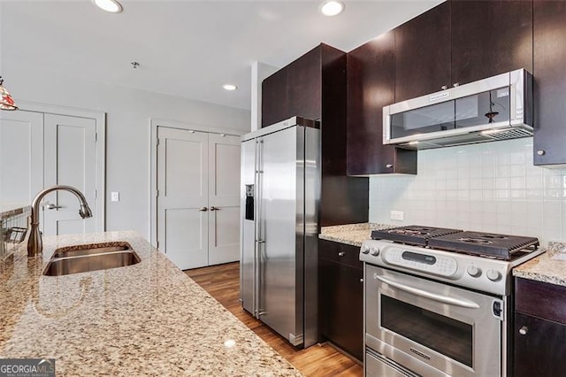 kitchen featuring light stone counters, high end appliances, sink, and tasteful backsplash