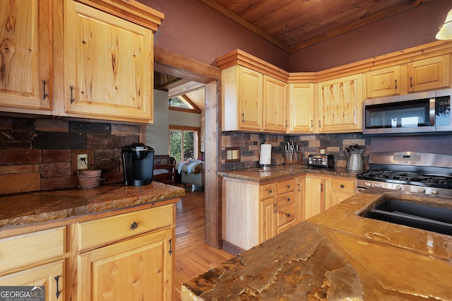 kitchen featuring decorative backsplash, stainless steel appliances, light brown cabinetry, and vaulted ceiling