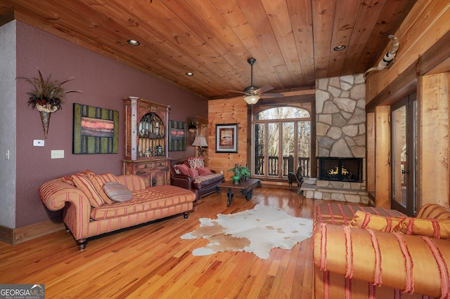 living room featuring ceiling fan, light hardwood / wood-style floors, a stone fireplace, and wood ceiling