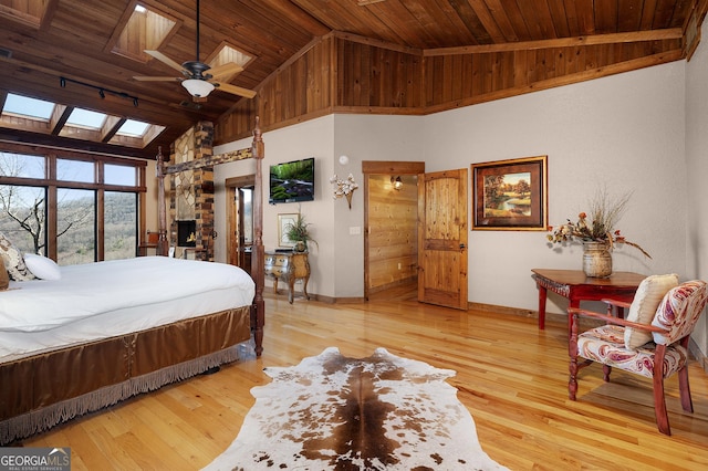 bedroom featuring a skylight, light hardwood / wood-style flooring, high vaulted ceiling, and wooden ceiling