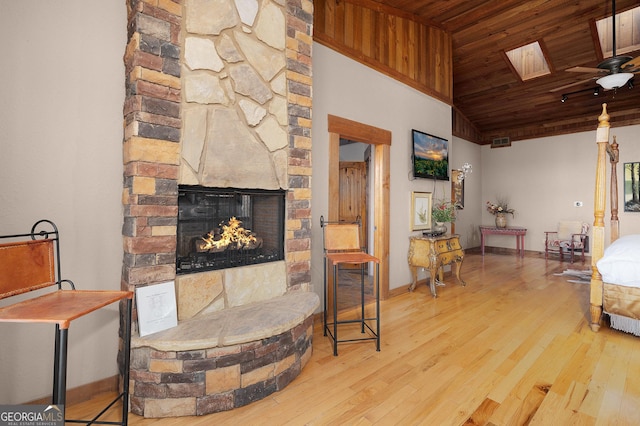 living room featuring lofted ceiling with skylight, ceiling fan, light hardwood / wood-style flooring, wooden ceiling, and a fireplace