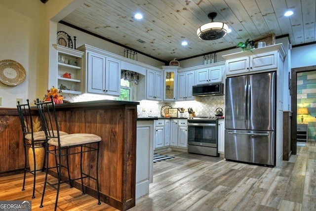 kitchen featuring kitchen peninsula, light wood-type flooring, appliances with stainless steel finishes, tasteful backsplash, and white cabinetry