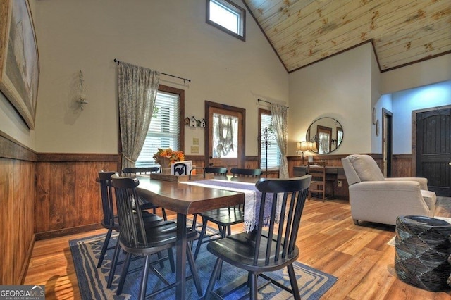 dining space with wood walls, wooden ceiling, high vaulted ceiling, and light hardwood / wood-style flooring