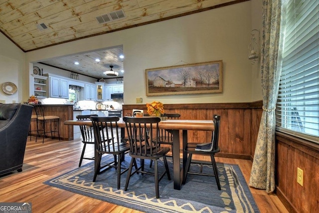 dining area with wooden ceiling, light hardwood / wood-style floors, crown molding, and wooden walls