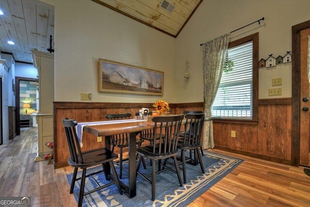 dining room featuring hardwood / wood-style floors, ornamental molding, wooden walls, and vaulted ceiling