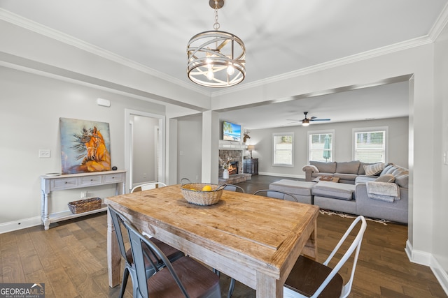 dining room with ceiling fan with notable chandelier, a stone fireplace, dark wood-type flooring, and crown molding